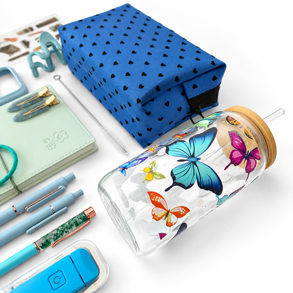 Butterfly glass cup with bamboo lid next to blue heart mesh pouch, mint notebook and pens
